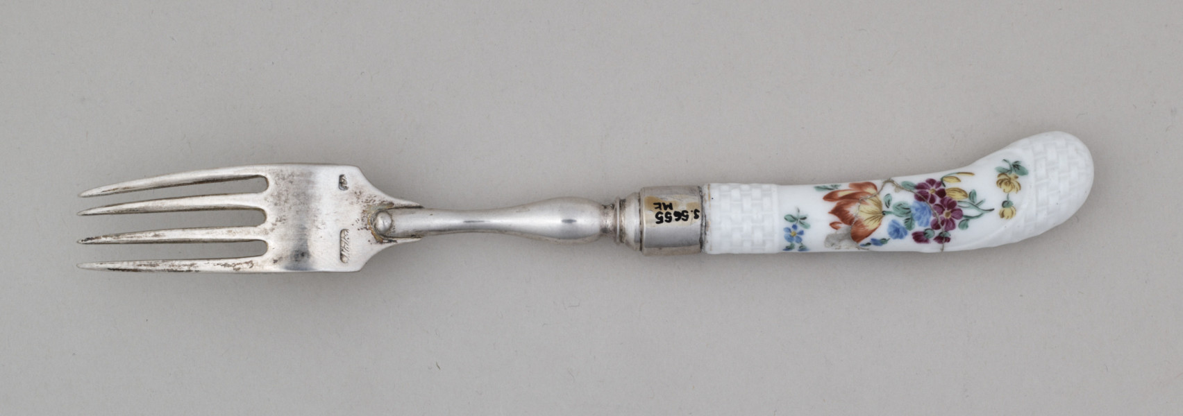 Widelec śniadaniowy, czterozębny. Zęby wygięte, zwężające się przy zakończeniu. Trzonek z nakładką ze srebra złoconego z białej porcelany
