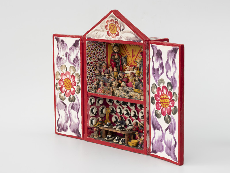 retablo - Ujęcie przodo ze skosu z prawej; Jasna, bogato dekorowana kolorowymi wzorami florystycznymi, prostopadłościenna, wewnątrz dwupoziomowa skrzynka (kapliczka) z dwuskrzydłowymi drzwiczkami, zwieńczona trójkątną koroną. Na wyższym poziomie pokazano Narodzenie Dzieciątka Jezus, gdzie wykonane z pasty ziemniaczanej i gipsu, polichromowane postacie Marii, Józefa i malutkiego Jezusa ustawiono na podwyższeniu. Bezpośrednio za Świętą Rodziną znajdują się zwierzęta: osioł i krowa. Poniżej głównych (nieco większych od pozostałych) figur zaprezentowano miejscową ludność (kobiety, mężczyzn i dzieci) w pozycji modlitewnej – większość klęczy z dłoniami złożonymi i skierowanymi ku Dzieciątku. Pierwszy rząd wypełniają najmniejsze figurki zwierząt hodowlanych: kóz, owiec, cieląt, jagniąt, krów, kur, źrebiąt oraz kota. Tło przedstawienia składa się z dwóch różnych dekoracji. Po obu bokach zastosowano wzór kropkowy (wielokolorowy) na białym tle, natomiast centralnie za postaciami namalowano usytuowane nisko na horyzoncie czerwone słońce na żółtym tle. Dolne piętro przedstawia scenę rodzajową: sprzedawcę kapeluszy w sklepie lub na targu w towarzystwie miejscowej ludności, instrumentów muzycznych i prawdopodobnie psa. Różowe tło wypełniono trzema rzędami figurek przedstawiających biało-czarne kapelusze typu panama.