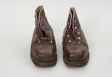 para trzewików - Ujęcie z przodu; Para damskich, brązowych, sznurowanych butów. Otwory na sznurówki zabezpieczone metalowymi obwódkami. Cholewka wykonana ze skóry licowej bydlęcej. To naturalna skóra, której zewnętrzna warstwa została poddana obróbce mechanicznej powodującej jej gładką fakturę. Między płaty skóry wszyte skórzane wzmocnienia na noski. Podeszwa zszywana. W wyniku zużycia skóry dosztukowane w latach późniejszych nowe warstwy kruponu z przodu podeszwy oraz fleki wykonane z gumy obuwniczej. Buty noszą ślady dużej eksploatacji, uszkodzenia skóry przy górnym zakończeniu buta oraz po całości widoczna popękana skóra.