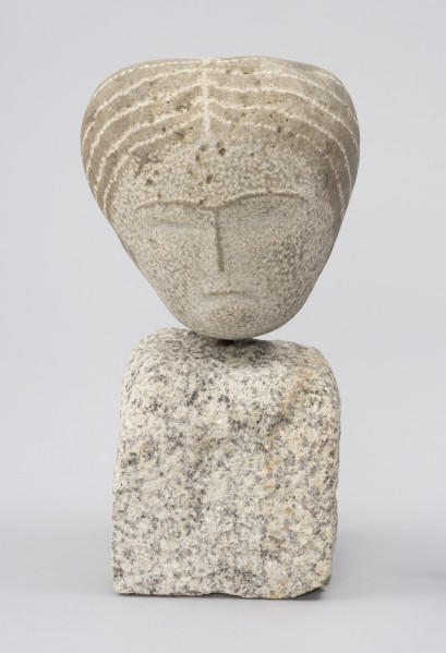 rzeźba; Prasłowianka I - ujęcie z przodu; Owalna bryła naturalnego kamienia polnego osadzona na kostce kamiennej. Skała tworząca głowę przekształcona w niewielkim stopniu. Rysy twarzy płytko cięte i przedstawione schematycznie. Wyraźna linia grzbietu nosa, rozwidlająca się na szczycie w łuki brwiowe powstała przez zachowanie cienkich pasów naturalnej warstwy zewnętrznej kamienia o ciemniejszym zabarwieniu. Podobnie wydobyto cechy fryzury - punktowym rytowaniem zaznaczony został przedziałek po środku głowy oraz linie wyznaczające szerokie pasma prostych, ciemnych włosów, biegnące od przedziałka do tyłu głowy, sugerując związanie w koński ogon.