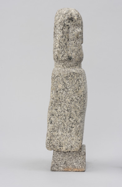 rzeźba; Polelum - ujęcie z prawej; Monolityczna, antropomorficzna pionowa forma o cechach ludzkich zredukowanych do prostopadłościennego korpusu i osadzonej na krótkiej szyi głowy. Figura ustawiona na nieco szerszym, kamiennym postumencie.