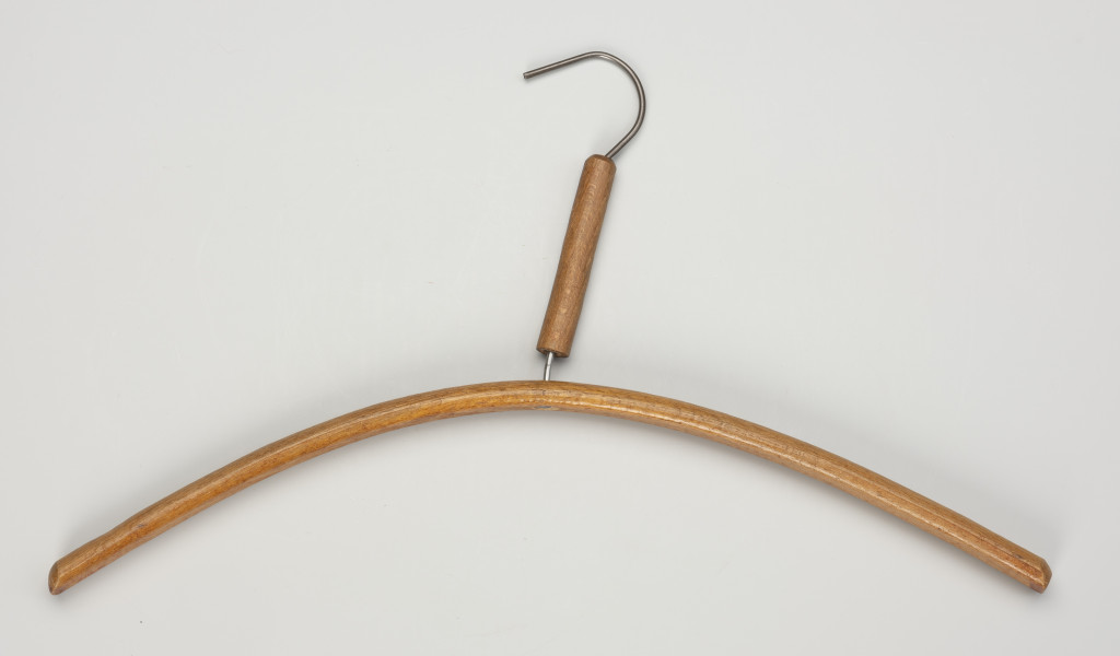 wieszak ubraniowy - Ujęcie z przodu; Drewniany wieszak na ubrania, płaski. Hak metalowy. Na pionowej części haka drewniana opaska.