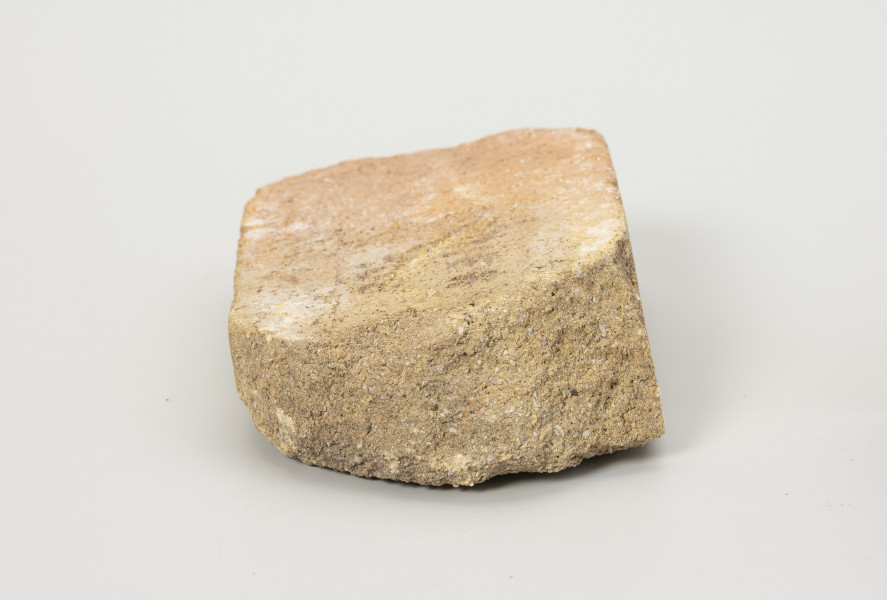 cegła szamotowa - Ujęcie z prawej; Prostopadłościenna cegła z jasnej glinki szamotowej. Widoczna strona obtłuczona. Cegła niejednolita, ziarnista.