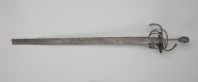 rapier - Ujęcie z przodu; Rapier o głowni prostej, obusiecznej, z ricassem. Na ricassie i krótkim odcinku głowni biegnie zaznaczone dwoma korytkami zbrocze. Sztych jest ułamany. Rękojeść ma krzyżowy jelec w esowatej formie i rozbudowany kosz do ochrony dłoni. Kosz składa się z trzech obłęków bocznych rozchodzących się ku ostrzu i osłaniających ricasso, po drugiej stronie są dwa obłęki boczne, z których górny jest większy, połączonych „oślą podkową” i dodatkowo dwoma obłękami. Trzon zwęża się ku końcowi, jego okładzina nie zachowała się. Głowica jest owalna, wydłużona z wyodrębnioną podstawą w formie pierścieni, ozdobiona jest wzdłużnie nacięciami i zakuta od góry.