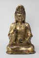 Bodhisattwa Guanyin - ujęcie z przodu; Duża, wykonana ze złoconego brązu figura przedstawia siedzącą w pozie medytacyjnej kobietę Bodhisattwę Guanyin (chin. 观音, sanskr. Awalokiteśwara, tyb. Czenrezig). Postać ma spuszczone, przymknięte oczy, symetryczną, pełną twarz o pogodnym i spokojnym wyrazie oraz gładko zaczesane włosy, schowane pod diademem i zaciągniętą na głowę tkaniną. Ubrana jest w długie, warstwowe, jedwabne szaty królewskie oraz wyszukaną, ciężką biżuterię książęcą: diadem, w którego centrum znajduje się niebiański Budda Amitabha (sanskr. Amitābha); pary dużych, okrągłych kolczyków ze spiczastymi zawieszkami oraz grubego naszyjnika z klejnotem, od którego odchodzi siedem pasów korali z wisiorkami. Jej prawa dłoń uniesiona na wysokości klatki piersiowej ułożona jest pionowo, jej środkowy palec i kciuk tworzą okrąg trzymając niezidentyfikowany, haczykowaty przedmiot. Poniżej znajduje się ustawiona poziomo lewa dłoń, która ściska niewielką wazę.