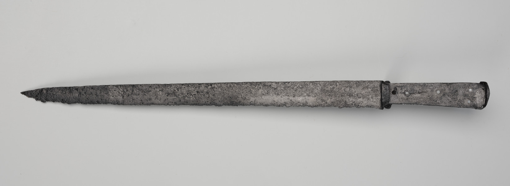 kord - Ujęcie z dołu; Głownia kordu jest prosta, jednosieczna, o sztychu decentrycznym. Trzon z jednostronnym wyżłobionym wgłębieniem ma cztery otwory do mocowania okładzin rękojeści, których brak. Trzon oddzielony jest od głowni nasadą. Głowica jest w formie kapturka, czyli cienkiej stalowej blaszki wygiętej w kierunku ostrza.