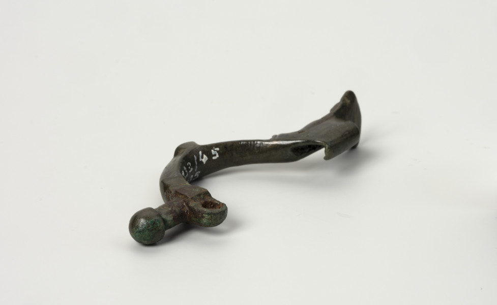 fibula z brązu z Borkowic typu Bügelknopffibel - Ujęcie z dołu; Zapinka z brązu z guzkiem na łukowatym kabłąku typu Bügelknopffibel. Fibula pozbawiona jest sprężynki i szpili.