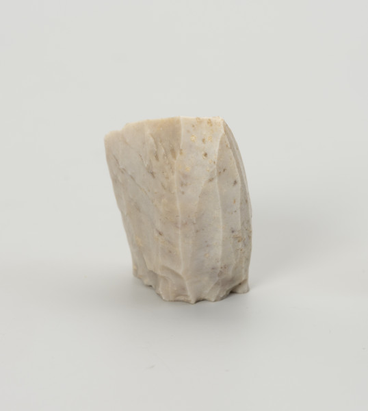 rdzeń stożkowy - Ujęcie z tyłu; Rdzeń z bryły krzemienia kredowego bardzo wysokiej jakości w końcowym stadium eksploatacji o znacznym stopniu redukcji uniemożliwiającym jego utrzymanie. Forma zbliżona do stożka lub ostrosłupa o dookolnej odłupni i płaskiej, lekko wklęsłej pięcie uformowanej jednym odbiciem. Widoczny na jednej ze stron duży negatyw wskazuje na naprawę rdzenia krótko przed zakończeniem eksploatacji. W masie widoczne są liczne długie egzoszkielety organizmów morskich, ułożone w podłużne linie. Zabytek w całości pokryty jest białą patyną wskazującą na długotrwałe zaleganie na powierzchni.