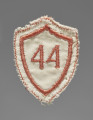Tarcza szkolna w formie naszywki wykonana z tkaniny w kolorze białym. Czworoboczna - z trzema rogami na górze i jednym na dole, każda krawędź zaokrąglona: górne do wewnątrz (do dołu), boczne na zewnątrz. Krawędzie obszyte nicią w kolorze czerwonym. W centralnym polu wszyty maszynowo nicią w tym samym kolorze numer ,,44’’ (nr szkoły).