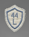 Tarcza szkolna w formie naszywki wykonana z tkaniny w kolorze białym. Czworoboczna - z trzema rogami na górze i jednym na dole, każda krawędź zaokrąglona: górne do wewnątrz (do dołu), boczne na zewnątrz. Krawędzie obszyte nicią w kolorze niebieskim. W centralnym polu wszyty maszynowo nicią w tym samym kolorze numer ,,44’’ (nr szkoły) oraz literę ,,L'' pod spodem.