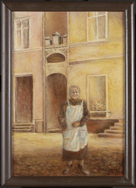 portret kobiecy - Portret uśmiechniętej staruszki w fartuchu, stojącej na ulicy, przed frontem kamieniczki. Ujęta w całej postaci, frontalnie. Ubrana w brązową sukienkę z długimi rękawami, na sukienkę ma nałożony biały fartuch z kieszeniami. W prawej kieszeni trzyma rękę, lewą rękę, lekko ugiętą trzyma przed sobą. Na głowie ma zawiązaną chustkę (?).
W tle front murowanej kamienicy – pokazanej do pierwszego piętra, w środku wejście do wewnętrznej uliczki, nad wejściem ozdobny łuk i krenelaż. Z lewej na parterze wysokie, brązowe drzwi wejściowe po schodkach, nad nimi dwuskrzydłowe okno, pod nim cienki gzyms. W prawej części na parterze duże okno wystawowe osłonięte pozioma poręczą, na wystawie kolorowe towary (nieczytelne). Dalej fragment szerokich schodów wiodących prawdopodobnie do wejścia. Wyżej cienki gzyms, nad nim dwuskrzydłowe okno. Ulica brukowana. Całość utrzymana w odcieniach brązów, żółcieni i beży.
Obraz w ramie.