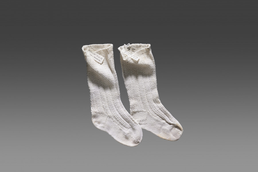 Para skarpet dziecięcych w kolorze białym/écru z widocznym ozdobnym ściegiem w formie trzech biegnących pionowo równoległych linii w równych odstępach. Wzdłuż górnej krawędzi wąski ściągacz. W części podeszwy oraz palców brak zdobienia.