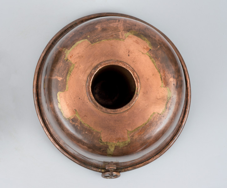 ujęcie z góry. Wierzch płaski, z otworem~kominem pośrodku. Kolor miedziany.