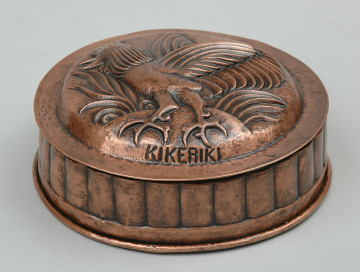 ujęcie 3/4. Naczynie w kształcie walca. Wierzch zdobiony półplastyczną dekoracją i napisem KIKERIKI.