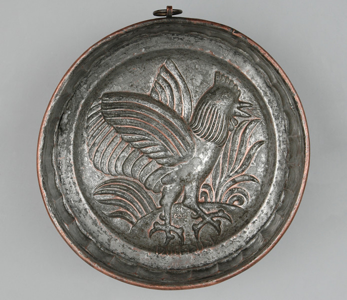 ujęcie z dołu (na wnętrze). W środku okrągłe, reliefowe pole, w którym kompozycja z kogutem o rozpostartych skrzydłach.