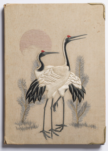 Na okładce papeterii na jedwabiu wyhaftowana para żurawi, dwie niskie sosny po bokach i tarcza słoneczna powyżej.

