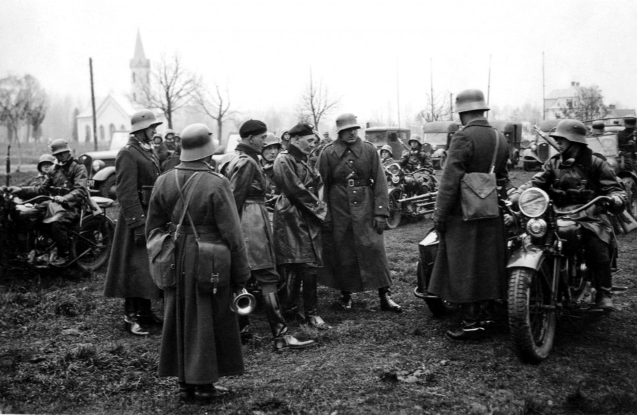 Zdjęcie przedstawia wizytację 10 PSK przez dowódcę 10 BK i szefa sztabu brygady. Oficerowie brygady noszą berety czarny wz.37 , kurtki skórzane, spodnie bryczesy i wysokie buty. Pułkownik (jak i jego strzelcy) noszą hełmy niemieckie wz. 1916, sukienne płaszcze i wysokie buty.