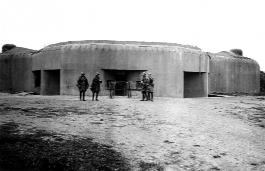 Zdjęcie ukazuje czterech żołnierzy stojacych przed bunkrem.
Mężczyźni są umundurowani w kurtki skórzane, wysokie buty i hełmy.