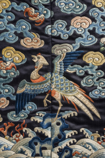 Na kwadracie jedwabiu wyhaftowany bażant z rozpostartymi skrzydłami stojący na skale. Wokół chmury. U dołu fale.
