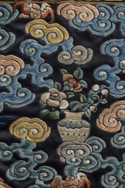 Na jedwabiu wyhaftowana waza z gałązkami kwitnących peonii. Wokół chmury.