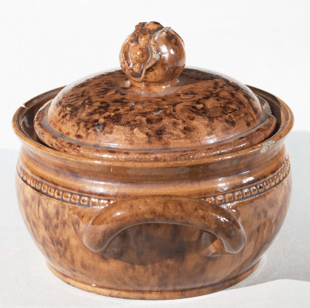 Miseczka okrągła z dwoma uchwytami i pokrywką. Pokrywka zakończona uchwytem w kształcie pąka kwiatu. Całość w kolorze wypalonej gliny