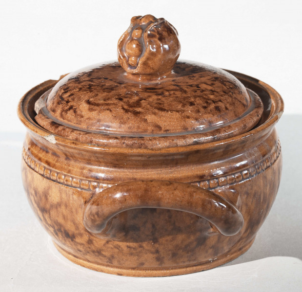 Miseczka okrągła z dwoma uchwytami i pokrywką. Pokrywka zakończona uchwytem w kształcie pąka kwiatu. Całość w kolorze wypalonej gliny