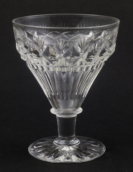 Kieliszek duży, wykonano ze szkła kryształowego
Stopa okrągła, nóżka krótka i szeroka, zakończona pierścieniem, na którym osadzona stożkowata czara. Spód stopy dekorowany płytkim szlifem o motywie wielopłatkowego kwiatka.
