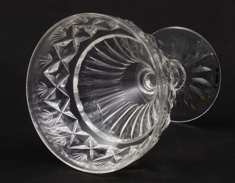 Stopa okrągła, nóżka krótka i szeroka, zakończona pierścieniem, na którym osadzona stożkowata czara. Spód stopy dekorowany płytkim szlifem o motywie wielopłatkowego kwiatka.