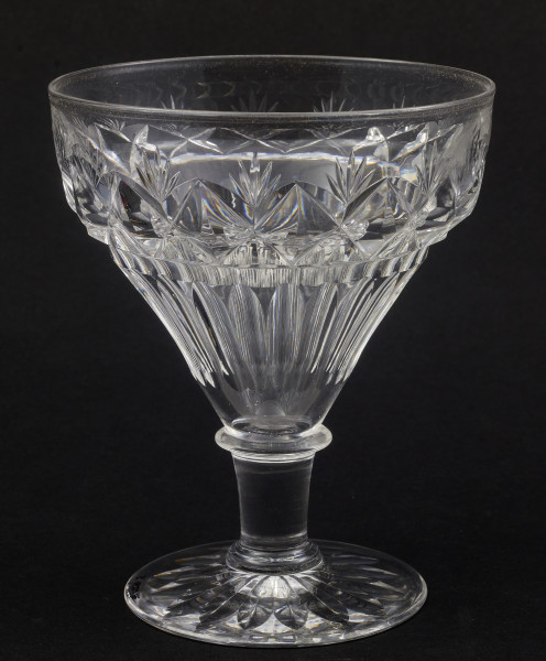 Stopa okrągła, nóżka krótka i szeroka, zakończona pierścieniem, na którym osadzona stożkowata czara. Spód stopy dekorowany płytkim szlifem o motywie wielopłatkowego kwiatka.