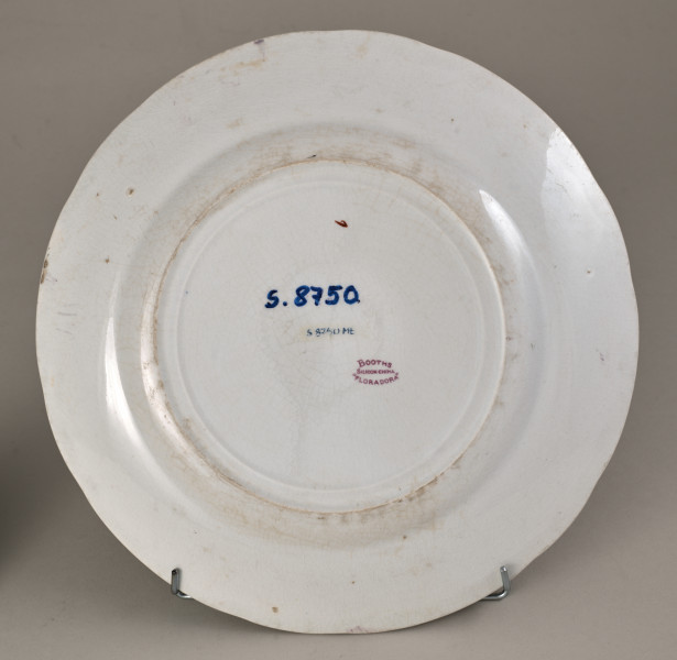 Stołowy, płytki talerzyk wykonany z białego fajansu. Zdobiony wielobarwną kalkomanią, złożoną z czterech jednakowych asymetrycznych roślinnych kompozycji