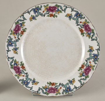 Stołowy, płytki talerzyk wykonany z białego fajansu. Zdobiony wielobarwną kalkomanią, złożoną z czterech jednakowych asymetrycznych roślinnych kompozycji